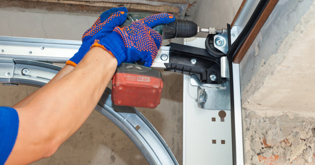Technician using a power drill to repair a garage door mechanism, showcasing local garage door maintenance expertise in Naples.